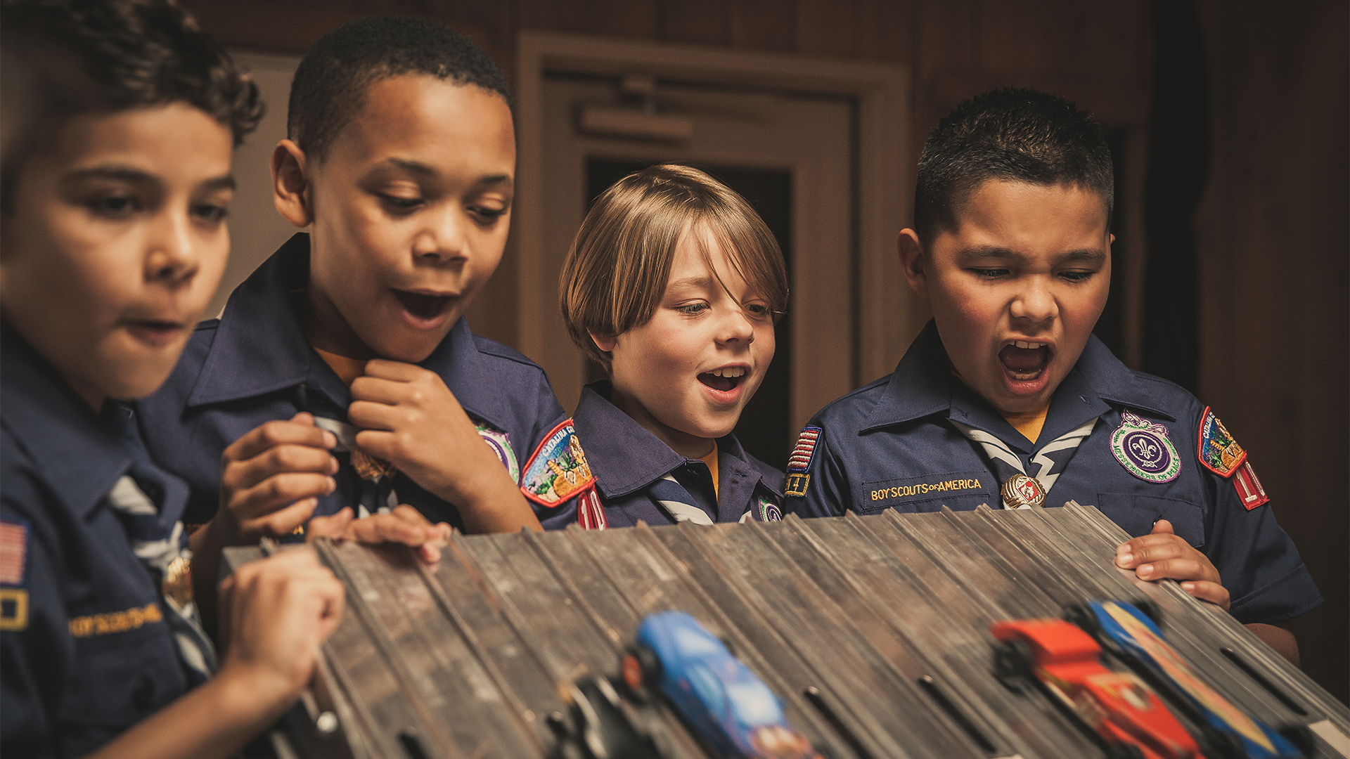 A group of Scouts cheering at several Pinewood Derby cars lined up to race down the track.