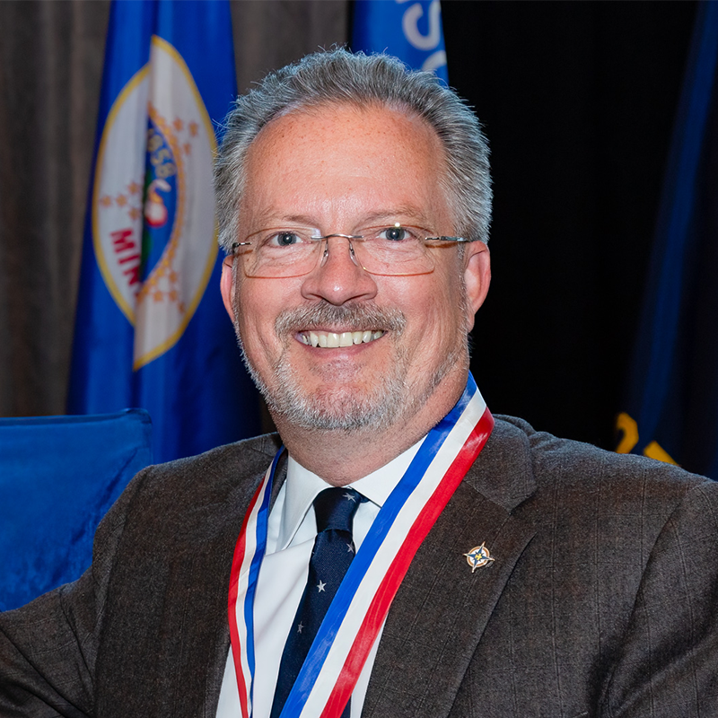 John Andrews smiling into the camera wearing a suit.