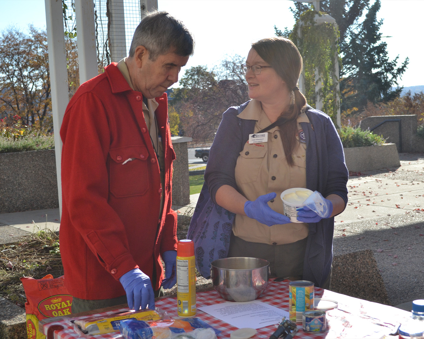 Two adults talk outdoors while surrounded by various cooking ingredients