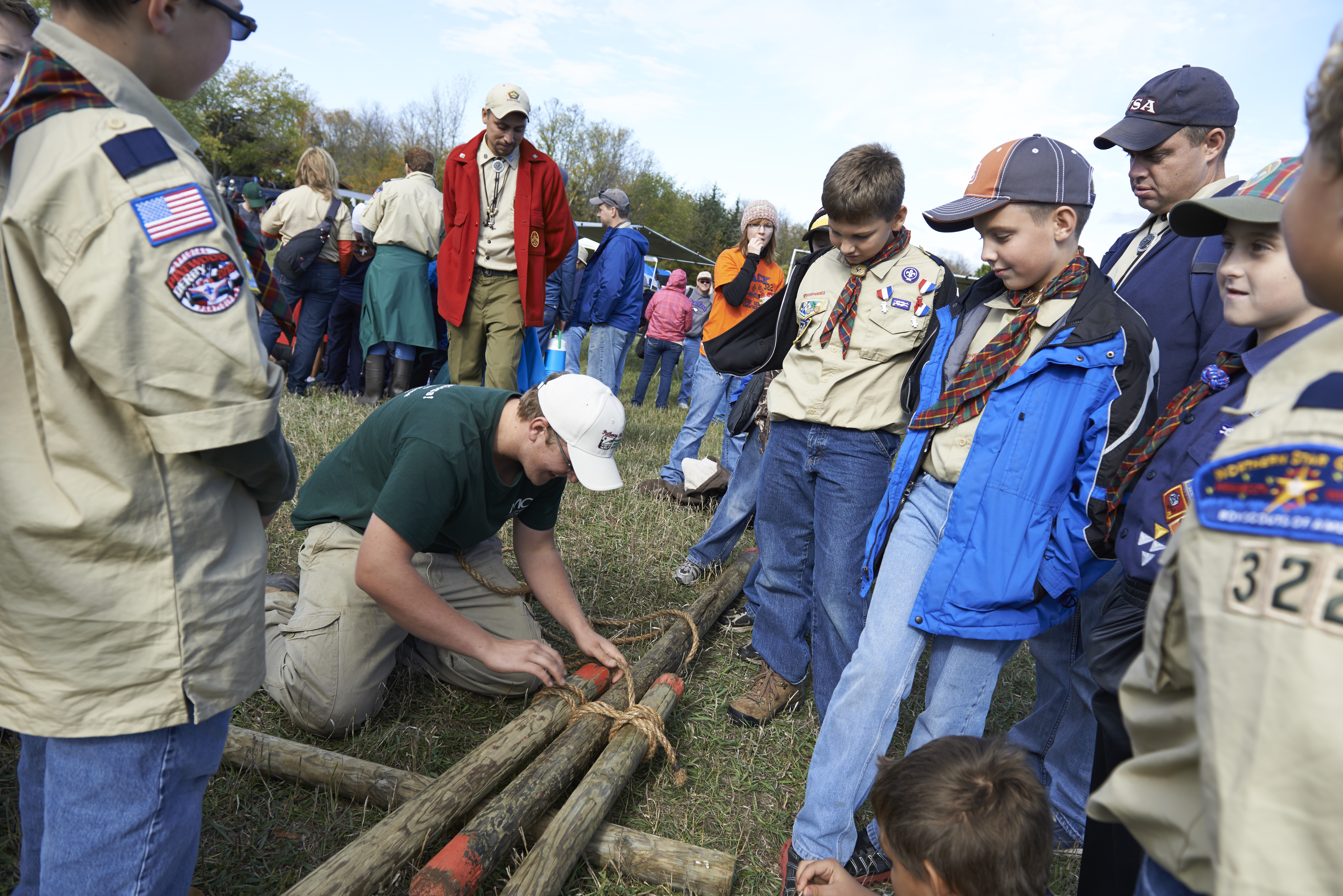 A group of Scouts watching a program counselor tie logs together. A group of Scouts watching a program counselor tie logs together.