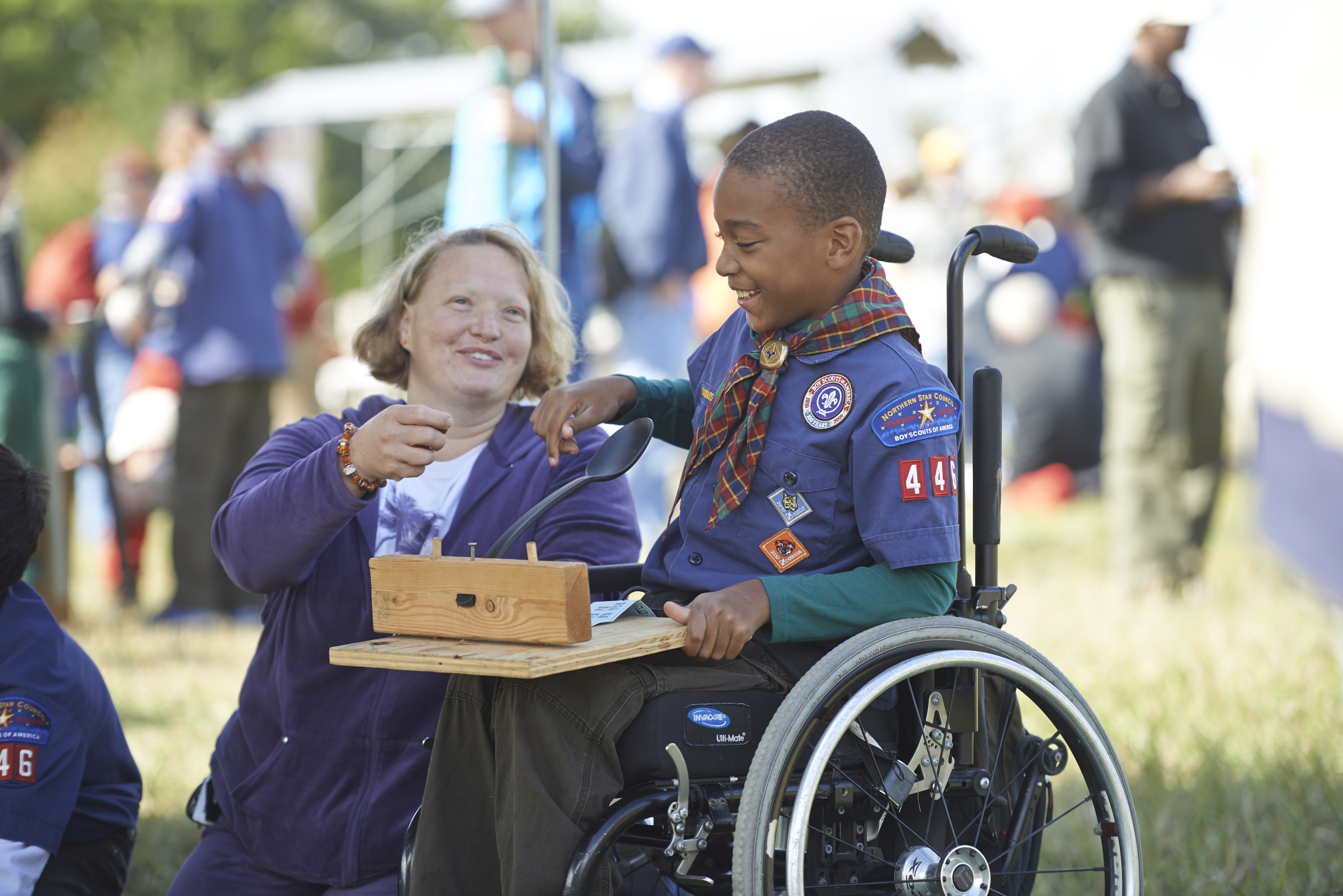 Cub Scout in wheelchair with guardian assisting him to launch catapult Cub Scout in wheelchair with guardian assisting him to launch catapult