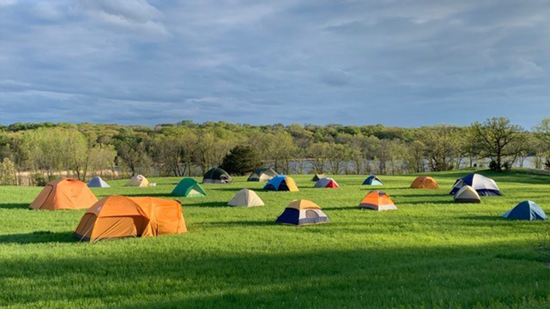 Twenty or so tents are set up in an open field near the lake