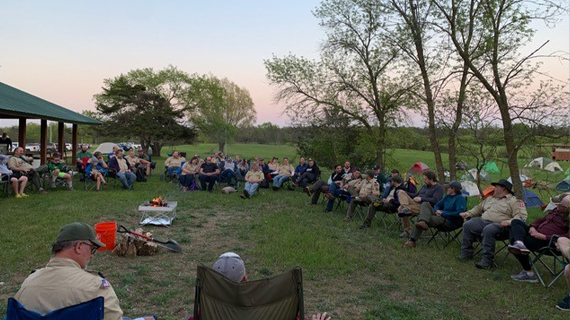 A large group of leaders are sitting in camping chairs in a circle around a campfire