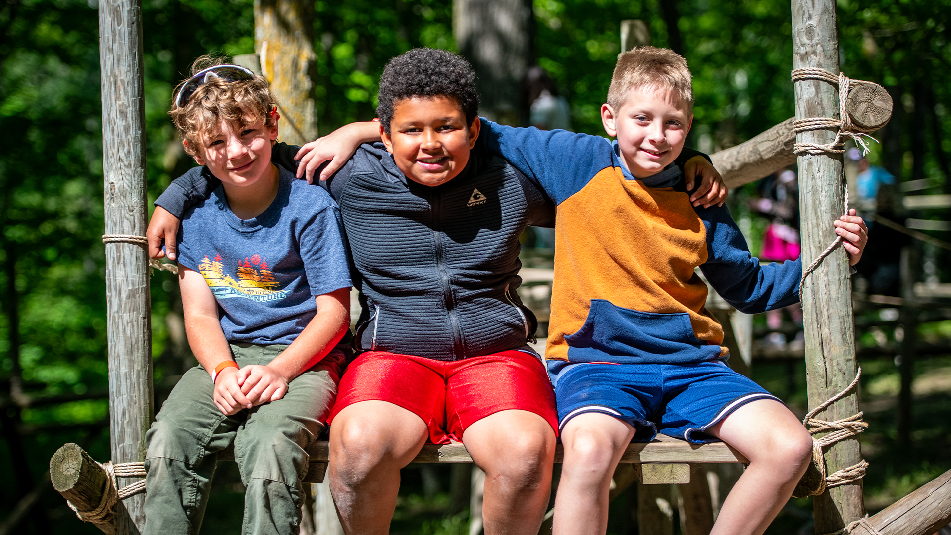 Three youth sitting on an outdoor structure and smiling