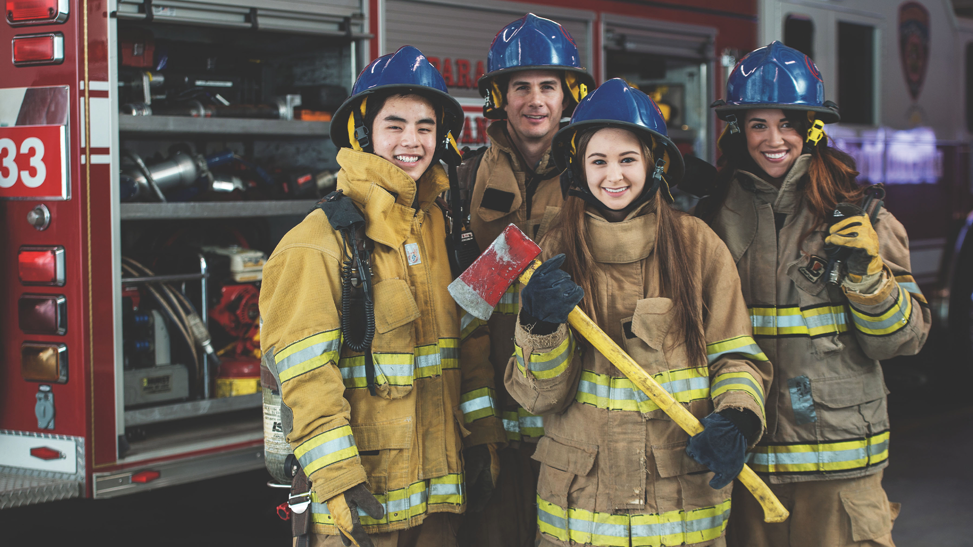 4 people all wearing firefighter uniforms pose in front of a fire truck. The two people in the back are professional firefighters, while the two in front are Explorer Scouts.