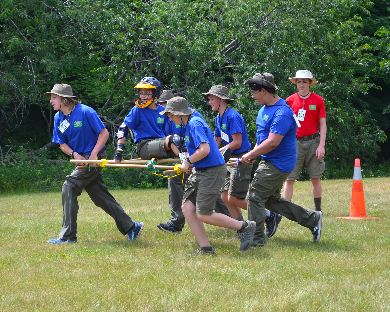 A group of 5 Scouts carry a simulated injured Scout on a hand-lashed stretcher while a staff member supervises