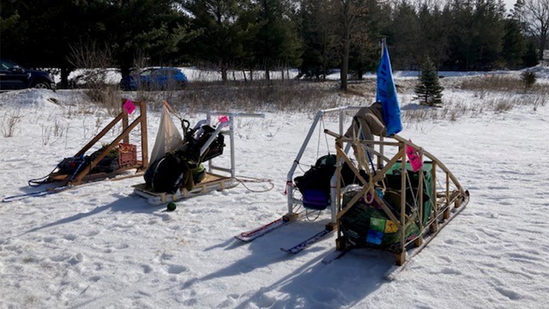 Four sleds of gear are packed and sitting on the snow while the Scouts are off doing an activity