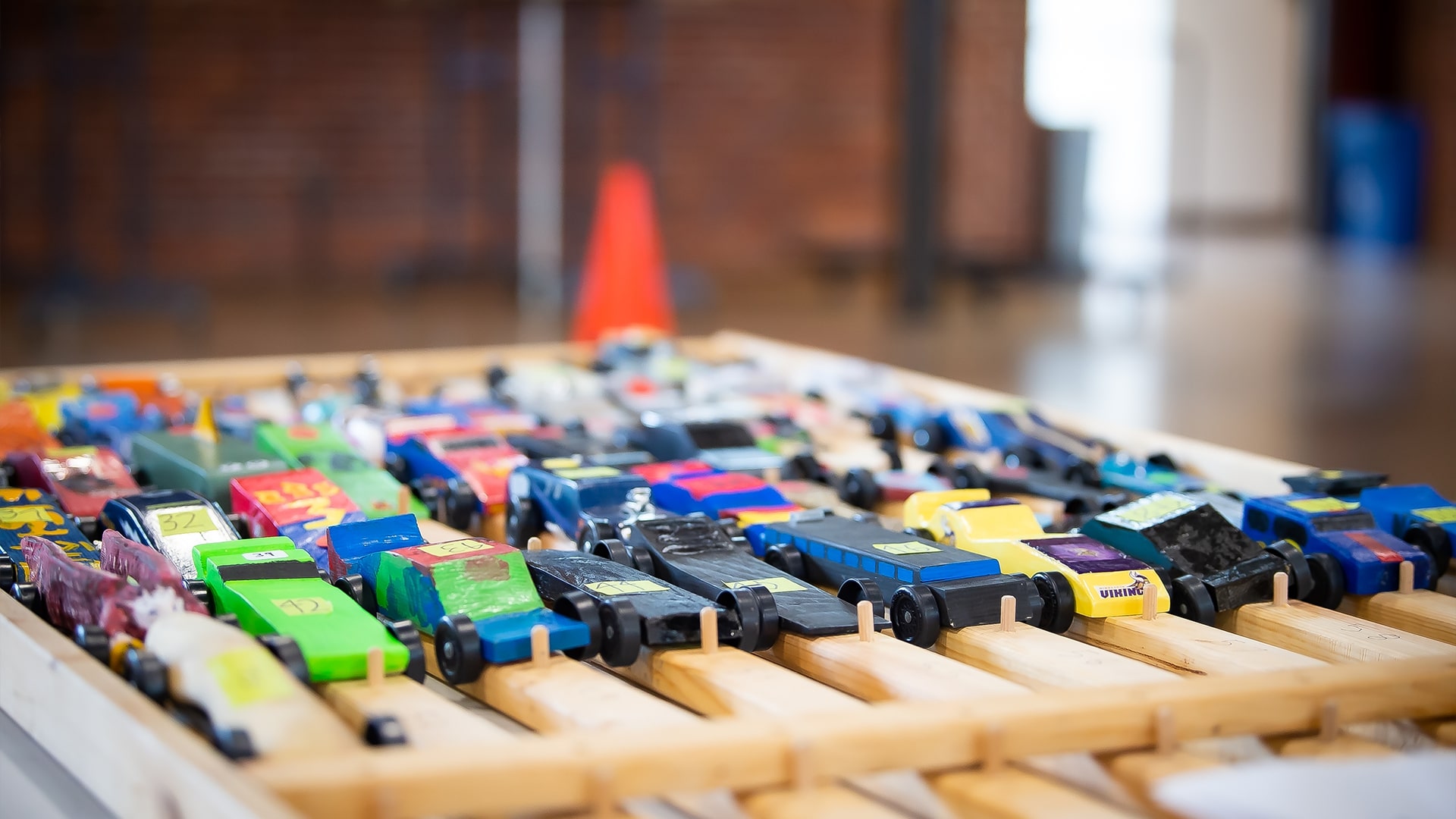 Thirty or so Pinewood Derby cars or all different colors, shapes, and designs are lined up waiting for their turn to race.